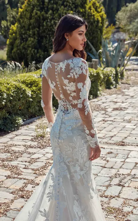 Back close up of Eddy K lace wedding dress with illusion back and long sleeves on bride standing in the garden looking to the side.
