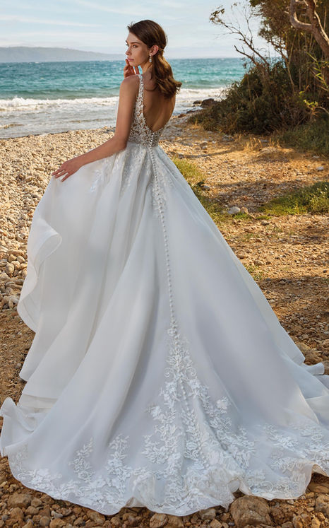 Back of Eddy k ballgown wedding gown with lace climbing the centre of the train on brunette woman standing by beach.