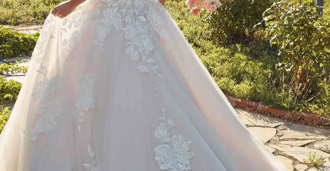 back of bride wearing wedding ballgown by wedding dress designer Eddy K with ivory lace and minimal beading over ivory tulle, lavender tulle & matte lining, unlined skin bodice, lavender buttons to end of train and drop waist. She is photograph in a beautiful garden.