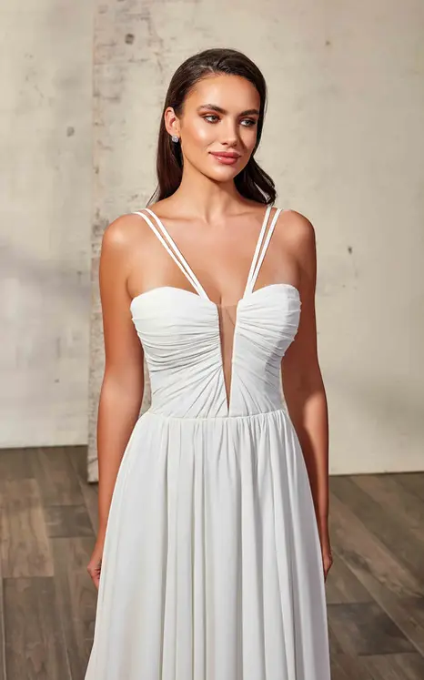 Close up of Eddy K crepe-chiffon wedding gown with ruched bodice, skin cleavage and double spaghetti straps on bridal model standing in a studio.