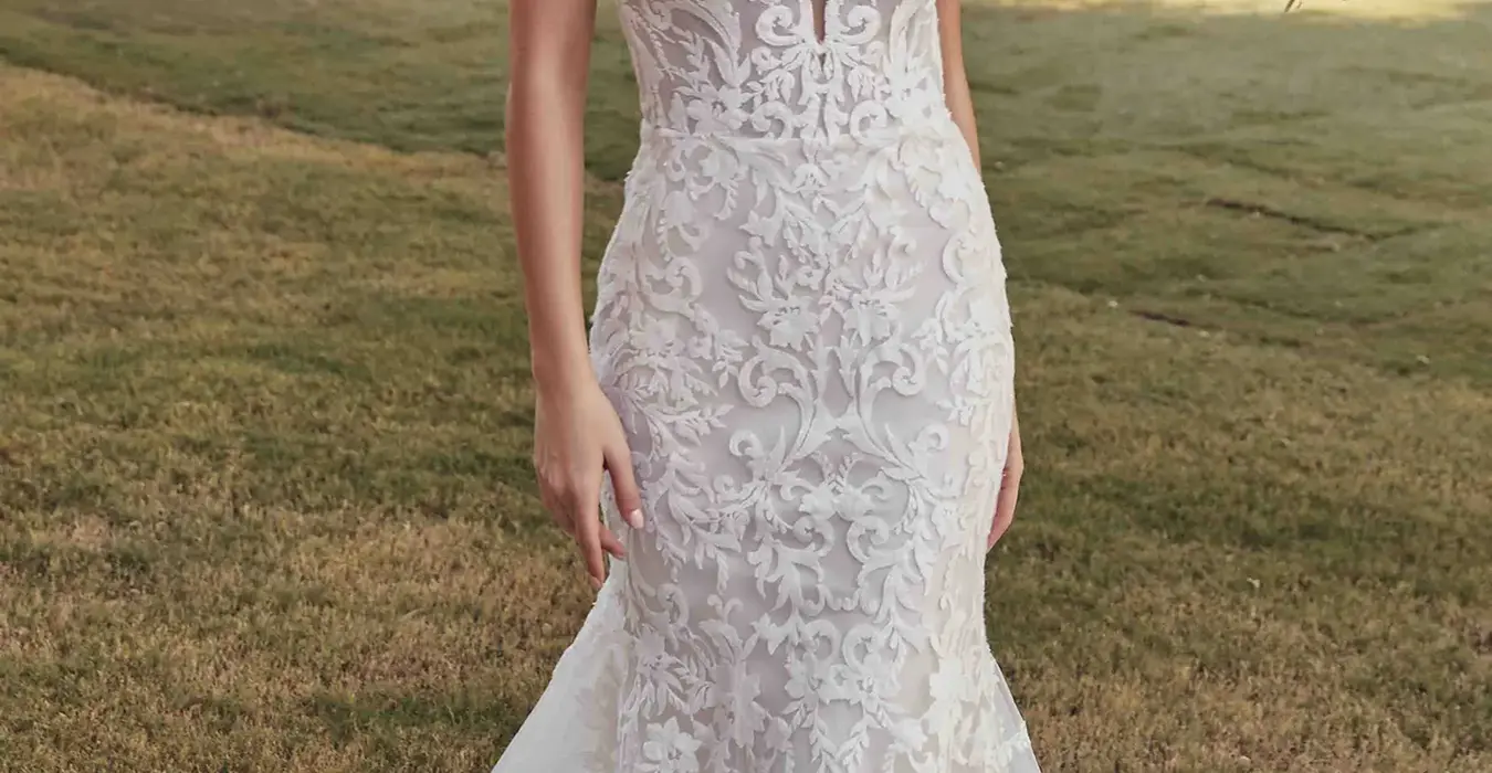 Eddy K fit-n-flare all over lace wedding dress with lace straps and skin cleavage on bridal model walking in greenery garden.
