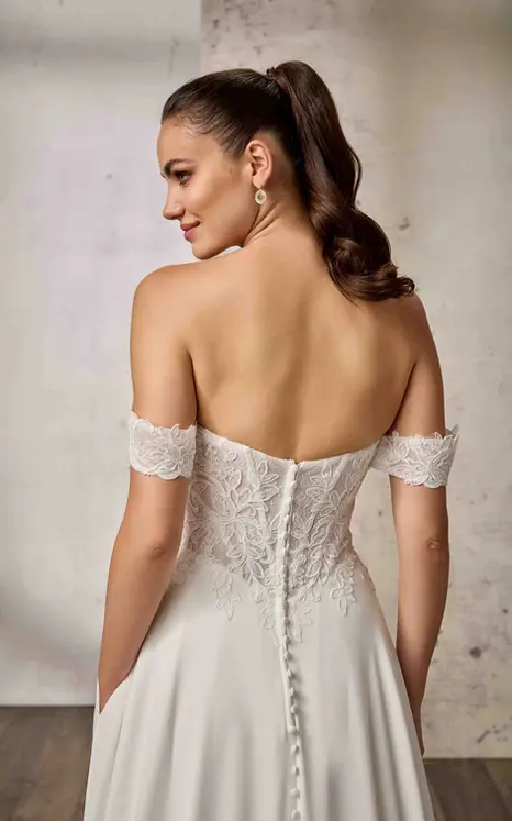 Back close of Eddy K lace a-line wedding dress with a sweetheart neckline and an off-shoulder bodice on a bridal model standing in an elegant studio.
