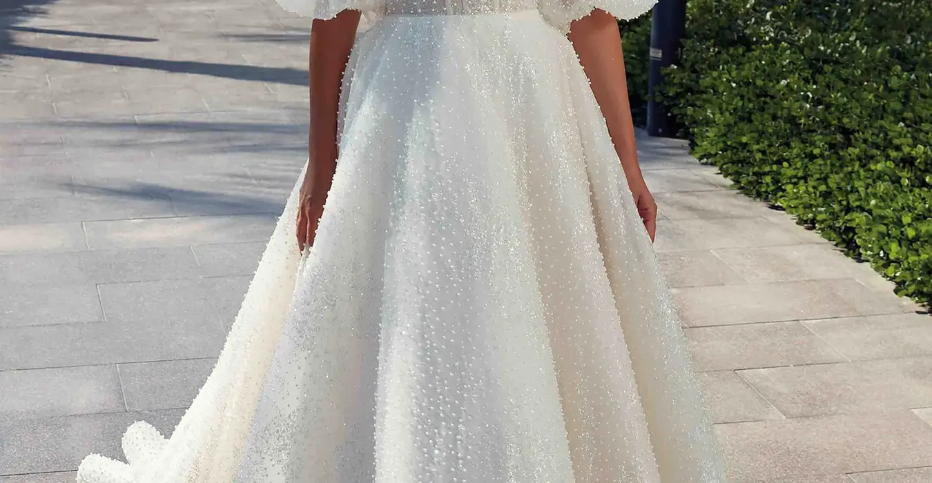 Bride wearing wedding ballgown by designer Eddy K with pearl beaded ivory tulle and glitter over champagne tulle, dust matte lining, unlined corset bodice, pearl buttons to end of train. She is photographed at a beautiful resort for a destination wedding