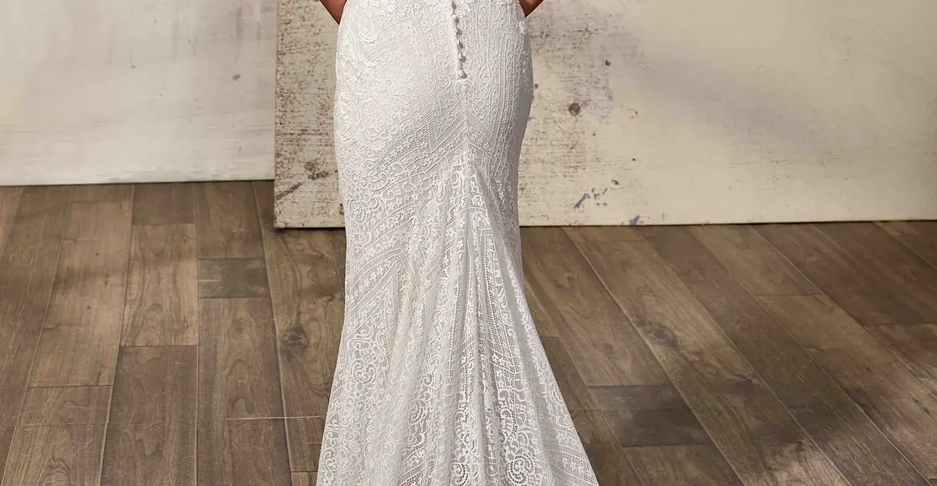 Back of Eddy K all over lace fit-n-flare wedding dress with key-hole back and open train on bridal model standing in a studio.