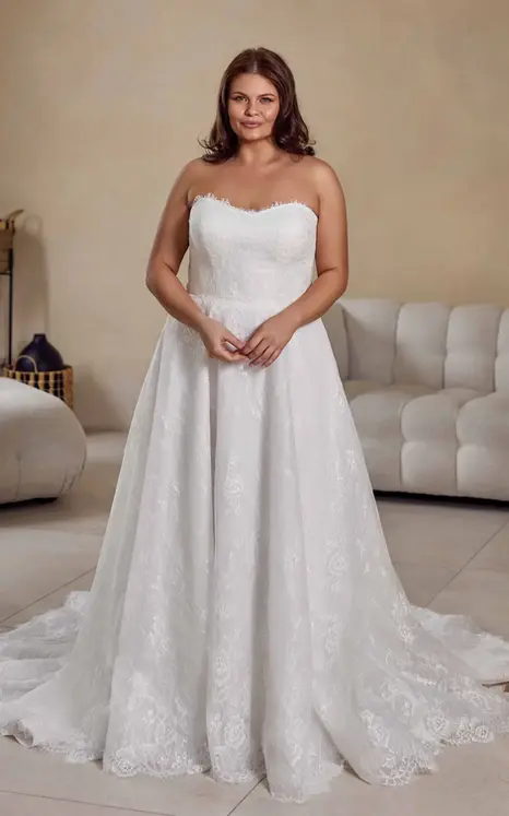 Eddy K lace ballgown wedding dress with a scoop neckline and a strapless bodice on a bridal model standing in an elegant studio.