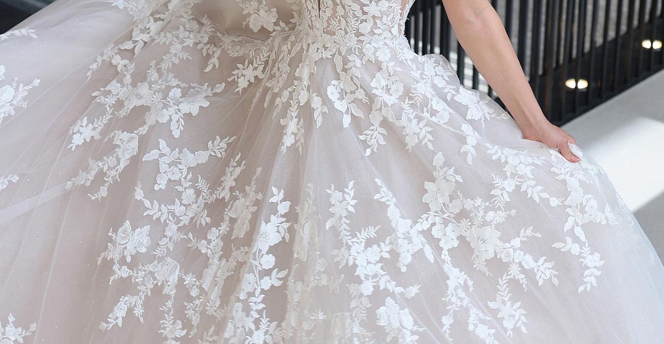 Eddy k a-line with v-neck neckline on fair skinned woman holding her skirt out standing in reception hall.