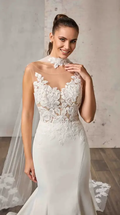 Close up of Eddy K satin mermaid wedding dress with an illusion neckline and a sleeveless body on a bridal model standing in bridal studio.