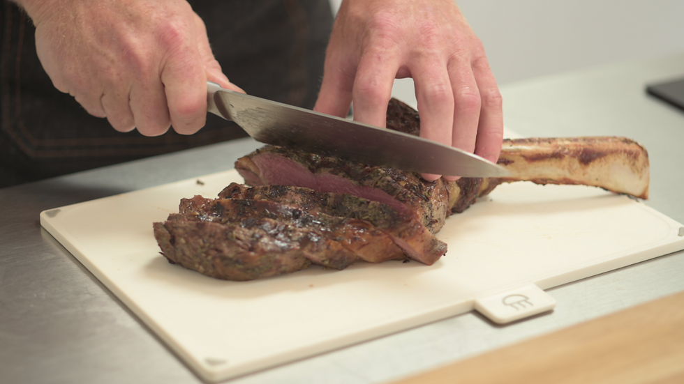 Chef guiding guest through slicing meat and preparing a gourmet dish.