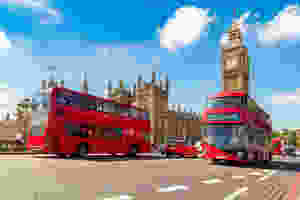 Westminster Palace towers over the streets of London with two red buses passing by.
