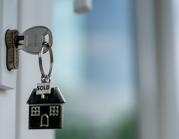 key in door with hanging keychain of a house that says "sold"