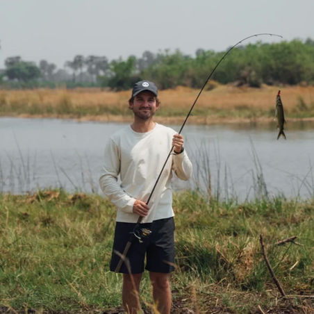 Man standing on land holding a fishing rod with a fish at the end of the line