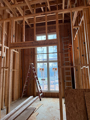 Framed building under construction with window installation in progress and ladders inside the unfinished structure.