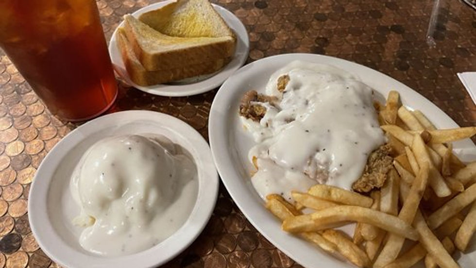 Plate of chicken fried steak topped with white gravy, served with French fries, a side of mashed potatoes with gravy, a slice of Texas toast, and a glass of iced tea at Texas Traditions Restaurant.