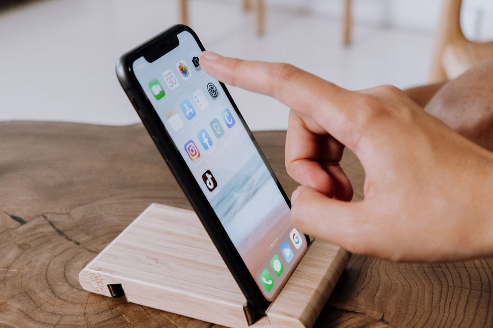 A person tapping on a smartphone screen while it rests on a wooden stand, displaying various social media app icons including