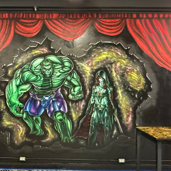 Large mural of the Hulk and Vision surrounded by red curtains, hand-painted by Hillie at his tattoo studio in downtown Gladewater.
