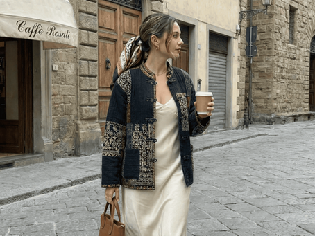 A fashion-forward woman walking down a European cobblestone street wearing an Anamica Fashion indigo and black patchwork quilted jacket styled over a cream silk slip dress.