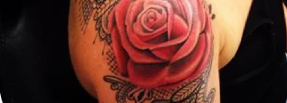 Woman's shoulder tattoo featuring a large red rose and ornate lace design