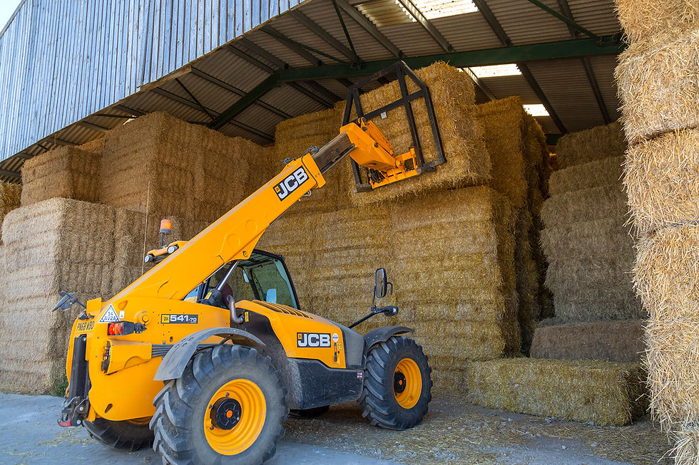 A JCB telehandler lifts a rectangular bale onto a stack.