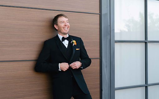 Groom buttoning jacket against a door for a portrait.