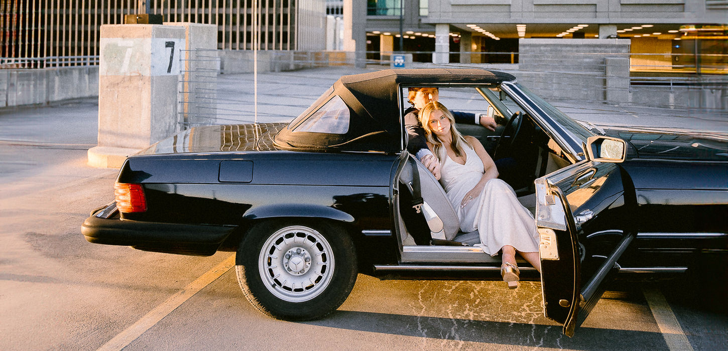 Couple posing in a black 1981 Mercedes 380 SL