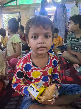 Young boy holding food, surrounded by other children, Eknai Subah Foundation