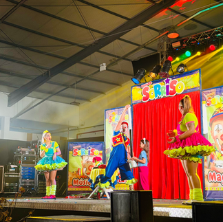 Fotografia do Palhaço Sorriso a atuar num espetáculo para crianças. O artista combina canções infantis, truques de magia e momentos de humor, criando uma experiência interativa e alegre que encanta o público familiar.