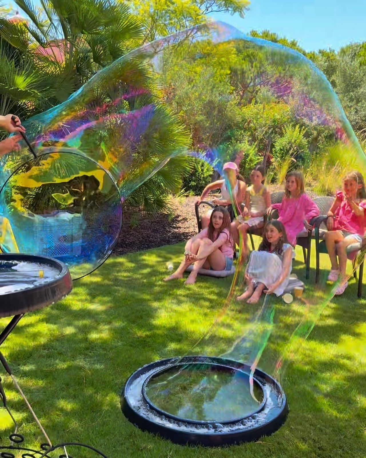 Espetáculo de bolhas de sabão gigantes da Magimax durante uma festa de aniversário, com crianças a assistir e a participar numa animação cheia de magia, diversão e interação.