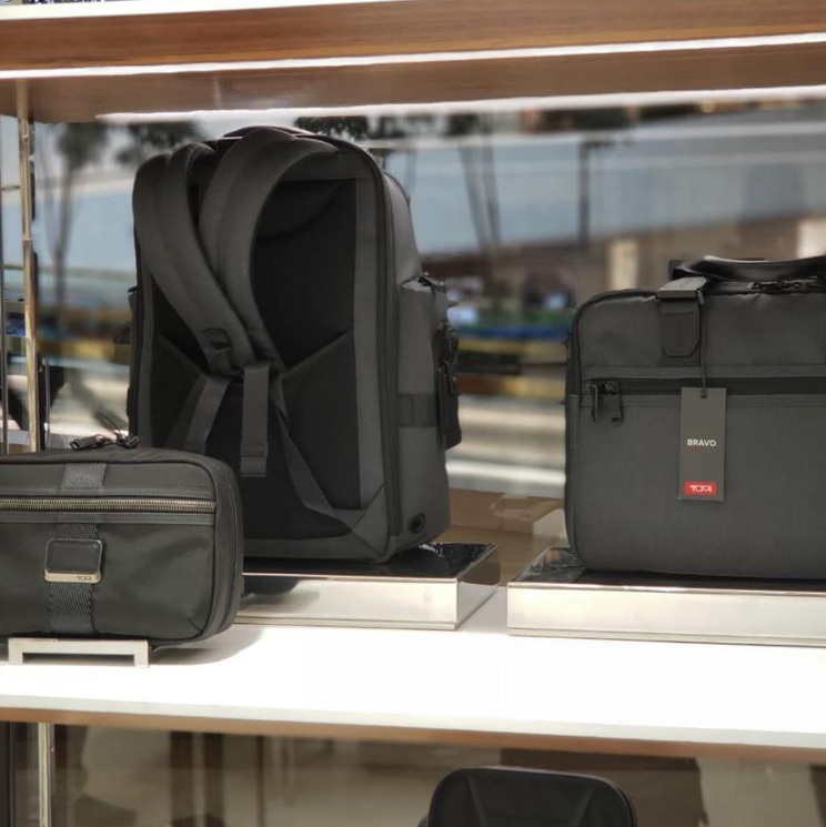 Nesta seção da vitrine, as plataformas de aço inox atuam como pedestais de precisão que elevam os acessórios da linha TUMI Alpha Bravo a um patamar de destaque individual.