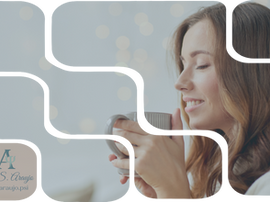 Mulher em primeiro plano, com fundo claro e desfocado, segurando uma xícara com as duas mãos próximas ao corpo. Ela mantém um leve sorriso, um dos olhos fechados, como se apreciasse o aroma da bebida, transmitindo sensação de pausa, presença e leveza emocional.