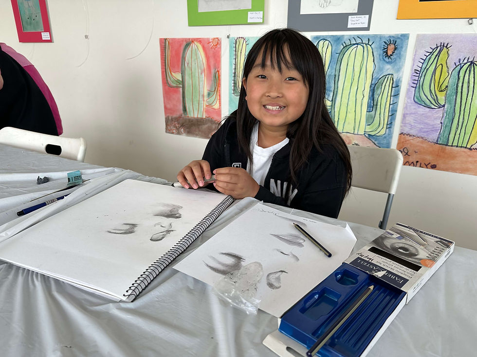 Young girl smiling while sketching at an art table.