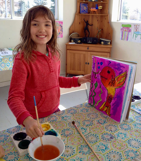 Young girl smiling while painting a colorful fish artwork.