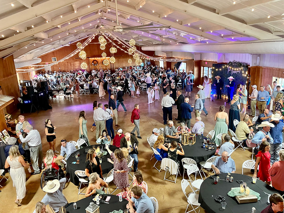 Guests at a large lively indoor wedding reception in a rustic chic hall, with people socializing and dancing. Warm, festive lighting; rustic but luxury atmosphere, largest venue in amarillo for large weddings.