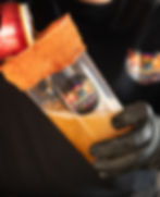 Persona con guantes negros sosteniendo un vaso de michelada con el logo de Drinkers.