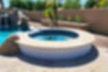Circular hot tub with decorative tiles next to a pool featuring a waterfall and rocks.
