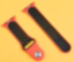 Two orange and black perforated smartwatch bands on a textured yellow background, showcasing perforations or fenestrations that allow moisture to evaporate
