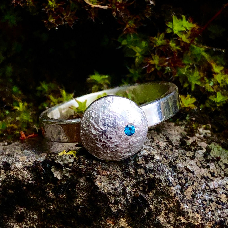 Thumbnail: A Lunar Moon Ring from Flying Silver Studio, with a blue topaz gemstone sitting on top of a rock.