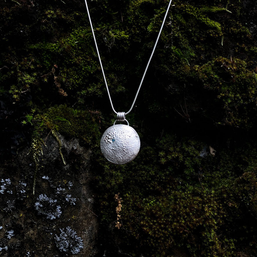 Thumbnail: A Lunar Full Moon Silver Pendant Necklace hanging on a mossy rock, made by Flying Silver Studio.