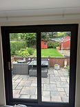 Sliding glass door opens to a garden with a lawn, paved patio, and wooden fence.
