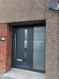 A black front door with glass panels, partially installed, tools and a drill on the floor nearby.