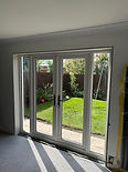 Open white French doors lead to a sunlit garden with a patio and lush greenery.