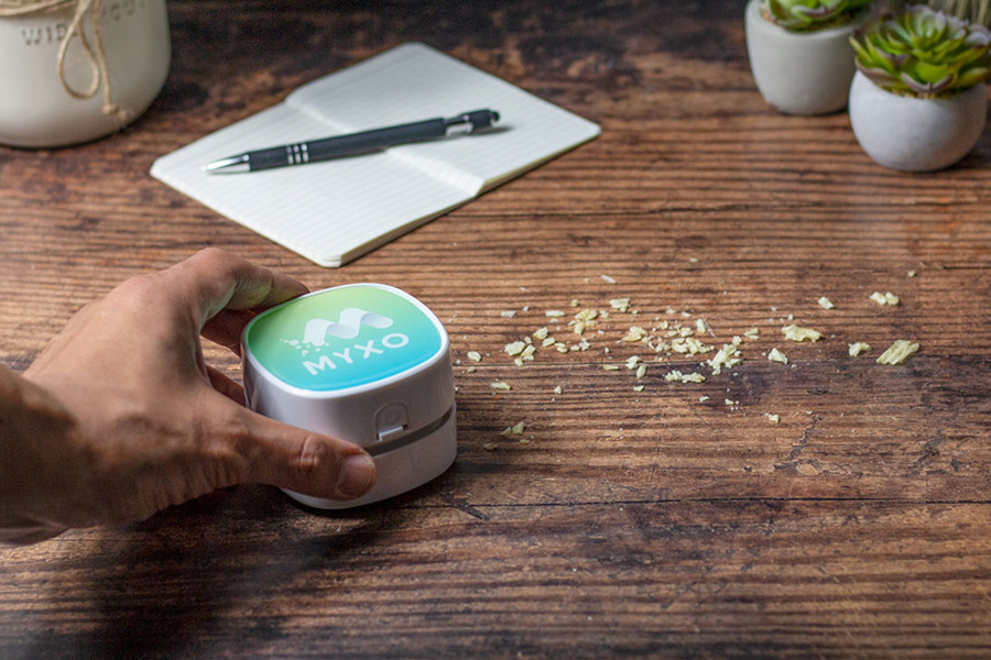 hand using mini desktop vacuum around a line of chip crumbs