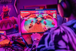 Person playing a video game on a laptop with a colorful game screen background.