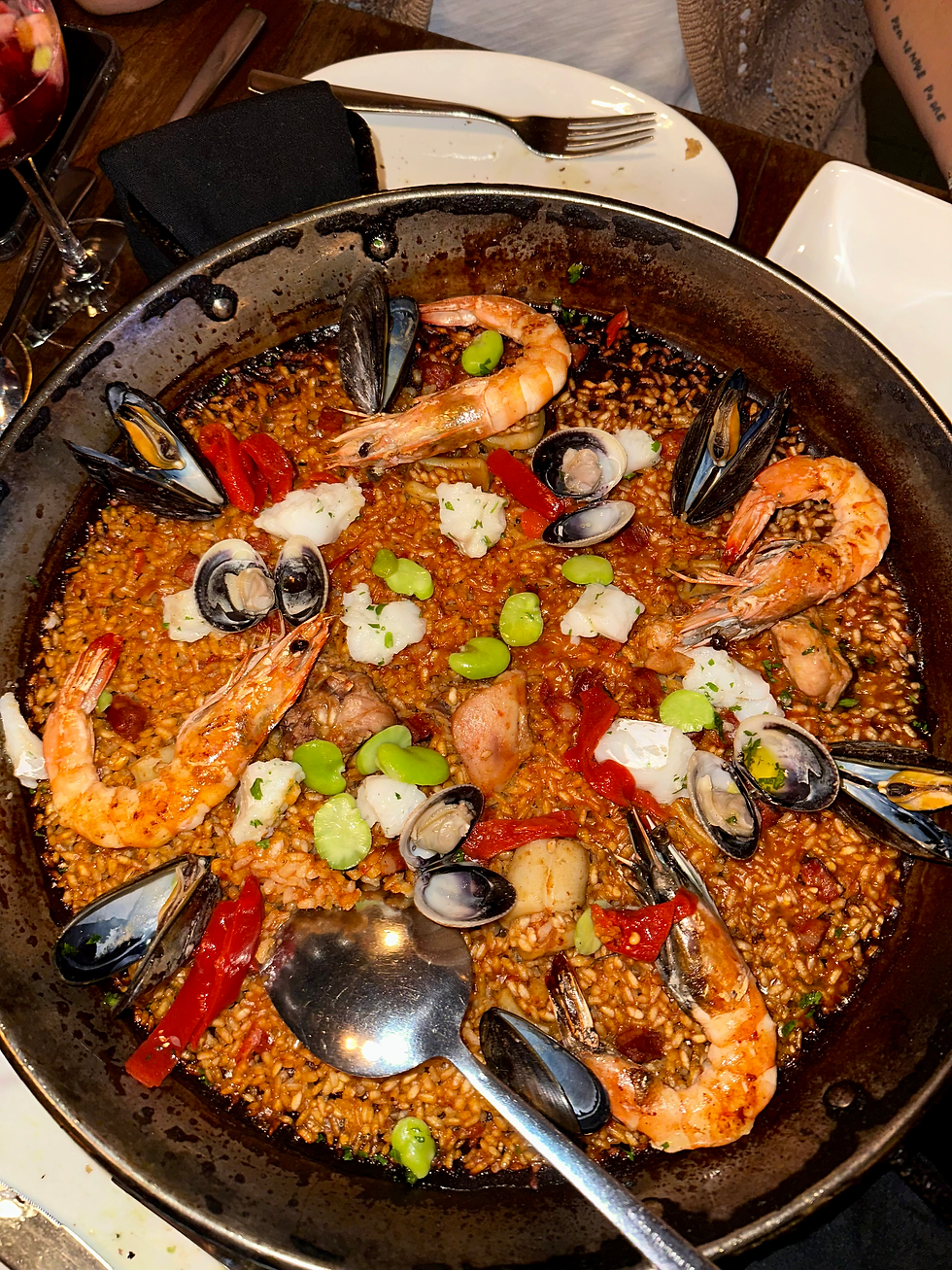 Classic Paella Socarrat being served, filled with rice, shrimp, mussels, chicken, chorizo, clams, white fish, squid, fava beans, peppers, and tomato sofrito.