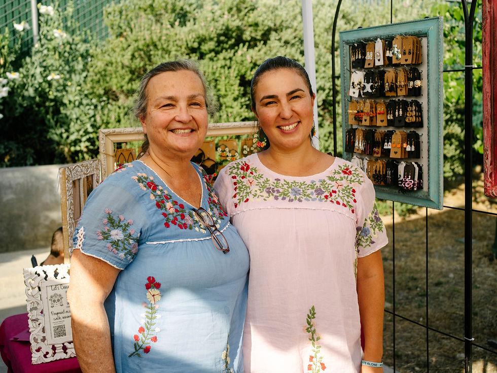 Two women smiling at vendor booth displaying handmade earrings.