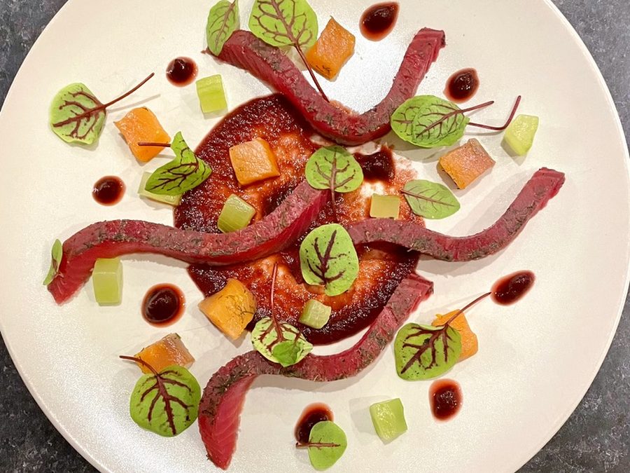 A plated starter of cured fish ribbons with red-veined sorrel, diced orange and cucumber, and dots of dark sauce