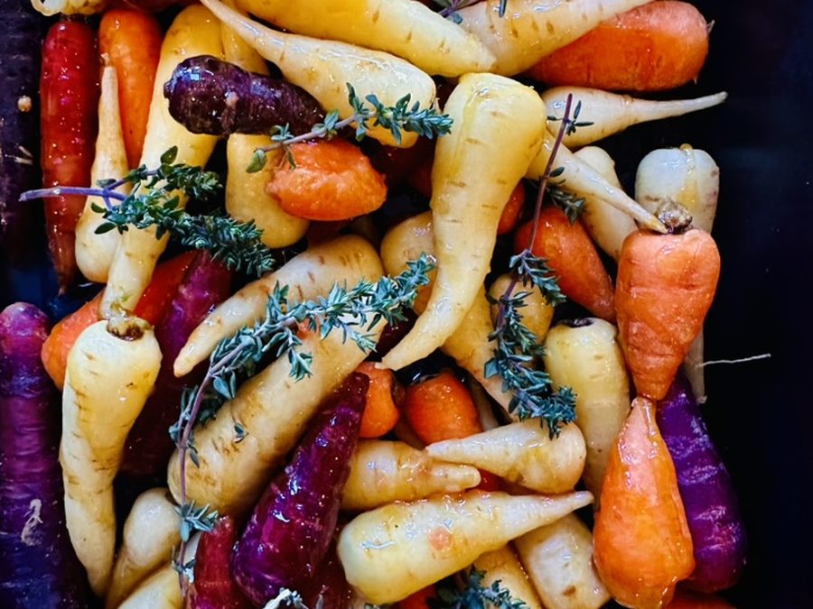 A tray of heritage carrots in purple, yellow and orange with fresh thyme and halved oranges