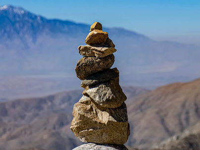 In the foreground a pile of stones in balance, with in the background a barren desert landscape and a distant mountain range under a clear blue sky.