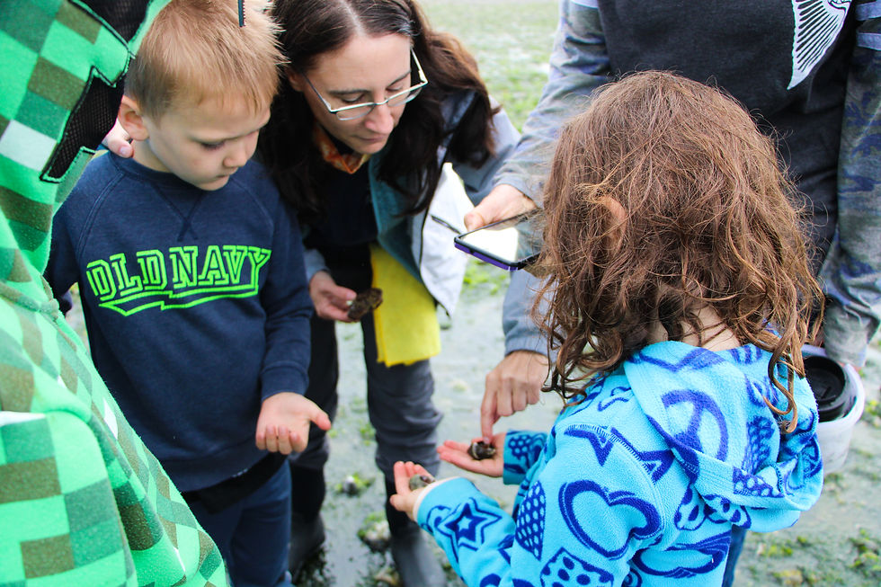 Woman pointing at snail in girls hand while children and adults look on.