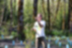 Man holds cedar sapling in front of blue tubes and forest.