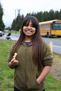 A girl holds up cheese in front of a bus.